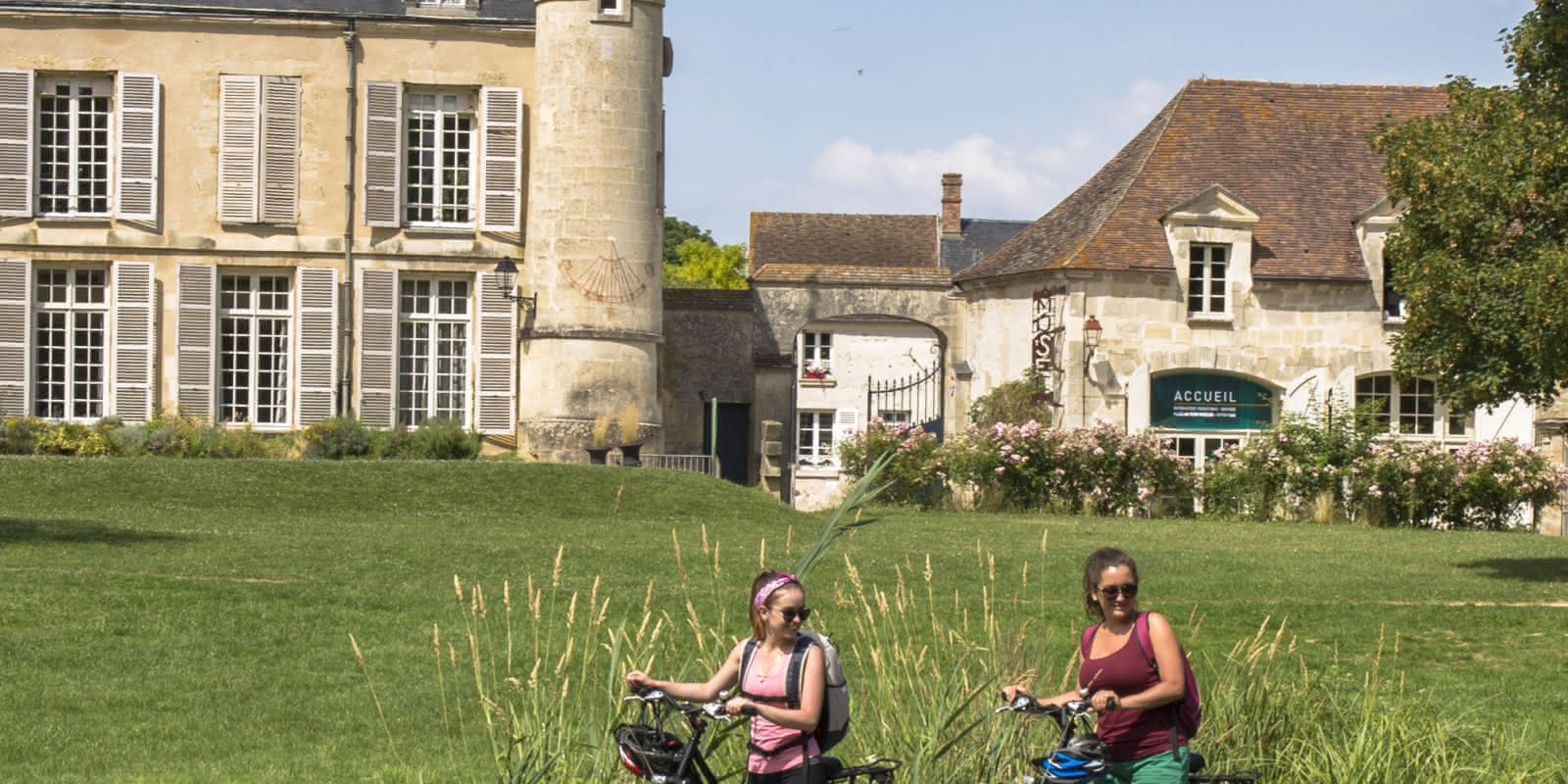 Photo de deux cyclistes en balade dans le parc de la Maison du Parc du PNR Vexin français à Théméricourt, Val-d'Oise (95). On y aperçoit le château de la Maison du Parc en fond, et en premier plan une randonnée à vélo.