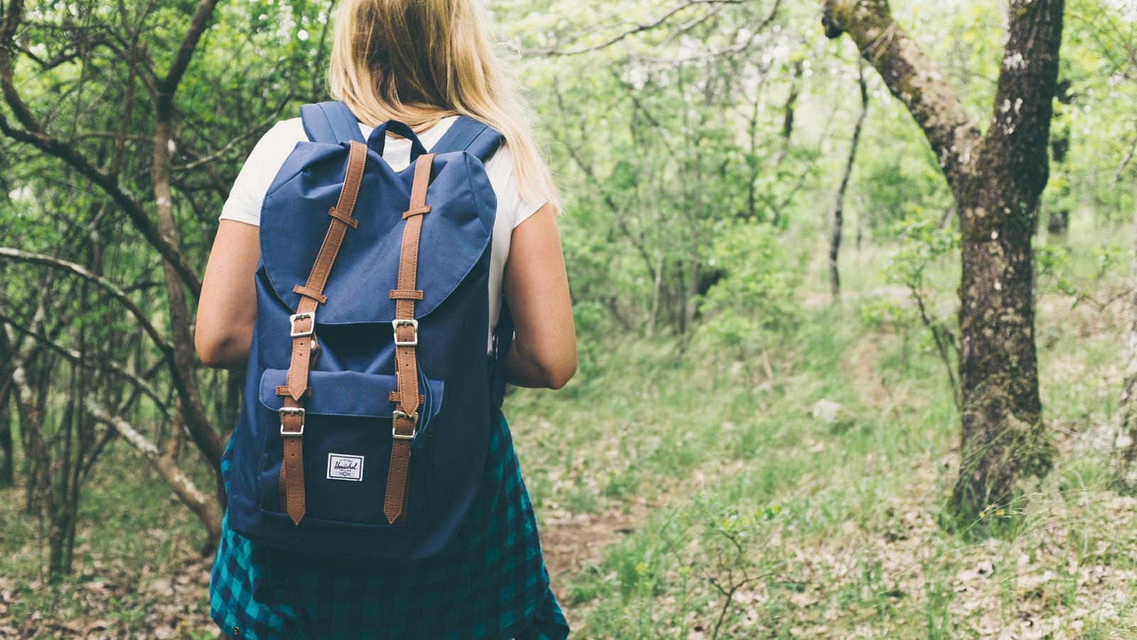 Photo d'une femme blonde portant un sac à dos bleu marine et une chemise à carreaux en train de randonner dans la forêt