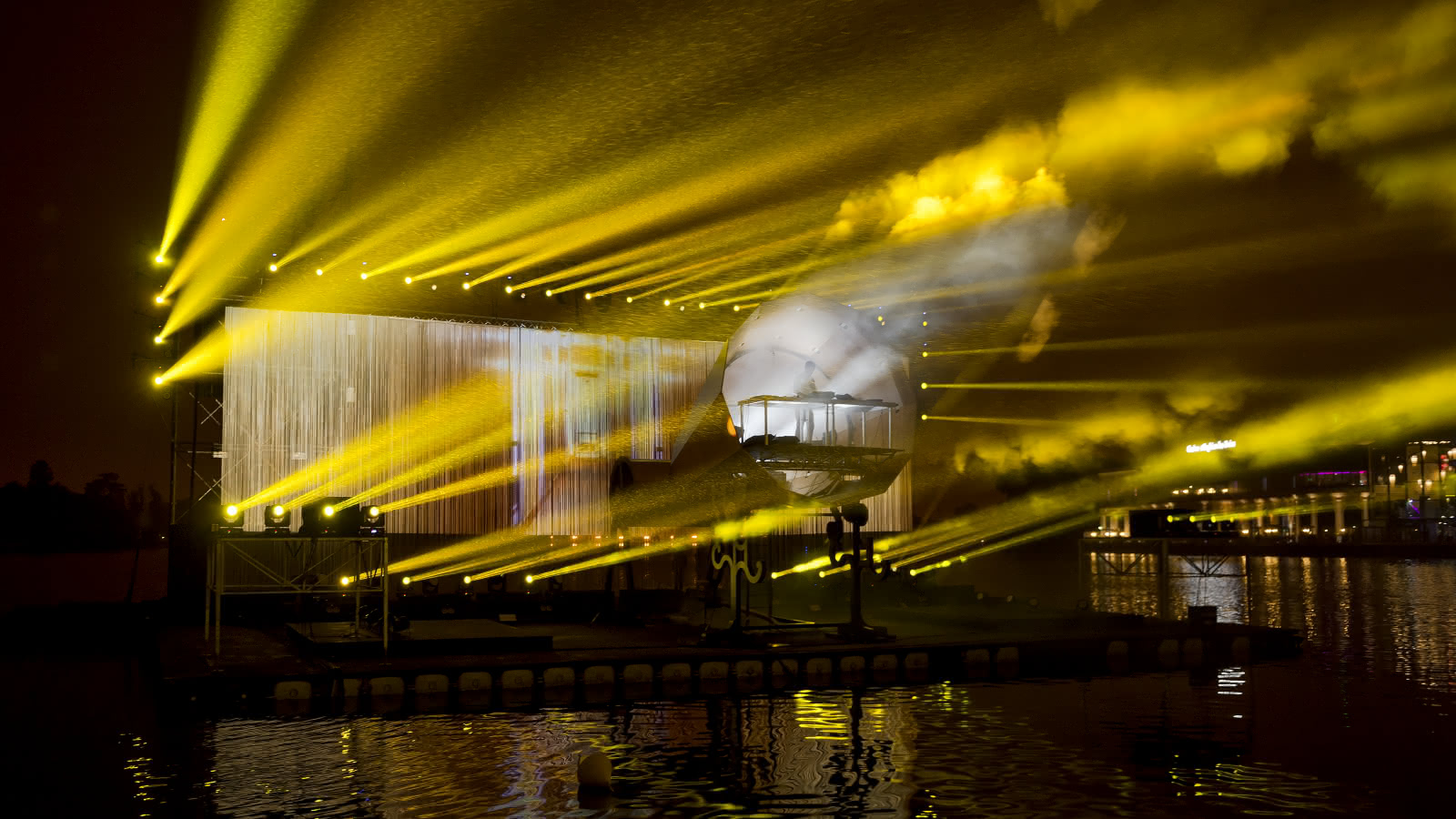 Photo de nuit de la scène flottante sur le lac avec phonogramme géant et lumières jaunes du festival des Bains Numériques d'Enghien les Bains dans le Val d'Oise